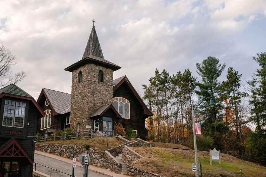 old church facade located on hilly terrain near autumn forest against cloudy sky
